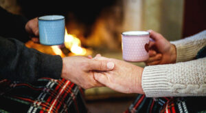 Cheerful mature couple celebrating Christmas holidays near fireplace