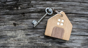 key with shaped house keychain on chain on wood texture background. Idea: buying a house, renting, selling real estate. Mortgage.